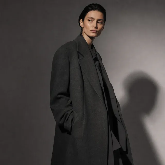 A model in an oversized wool coat under a single hard studio light